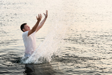 A young man standing on the waist in the sea created a wall of splashes with the movement of his hands