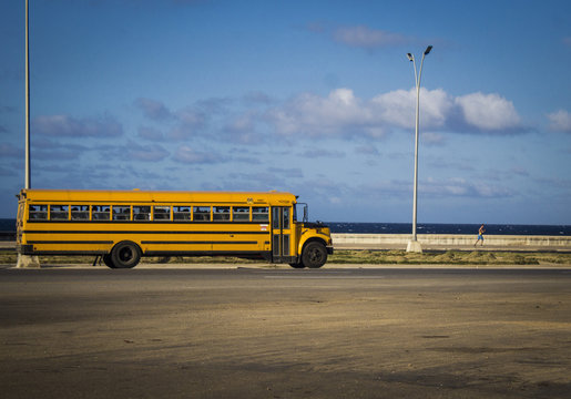 photograph of a very old school bus, from the 60s, crossing a highway that is next to the sea. Vintage concept
