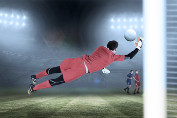 Fit goal keeper jumping up against large football stadium under blue sky