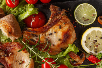 Fried pork chop on a black plate with spices, herbs and tomatoes.