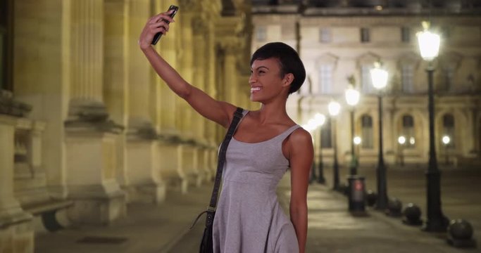 Smiling black female under lights at night taking selfies with her phone camera to post on social media, Pretty millennial woman takes photos  of herself on smartphone, 4k