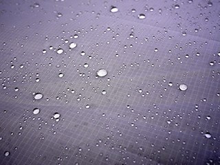 Photo of a grey tarp fabric with drops of water on it. Rain protection. Waterproof fabric.