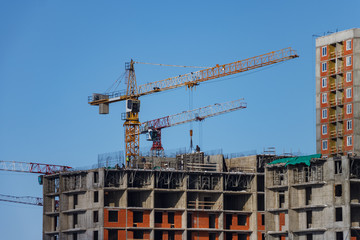 Workers and construction cranes install formwork for concrete walls. Builders are building a multistory apartment building. Monolithic construction