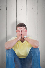 Casual man with head in hands against white wood