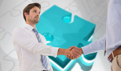 Two businessmen shaking hands in office against jigsaw