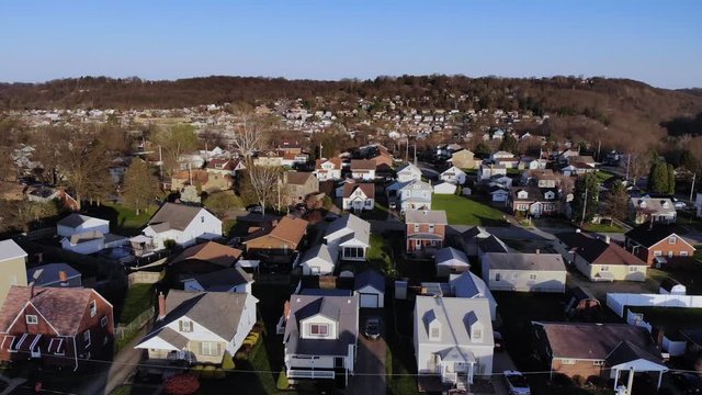A dusk early Spring slow forward aerial establishing shot of a typical residential neighborhood in a Western Pennsylvania small town. Pittsburgh suburbs.  	