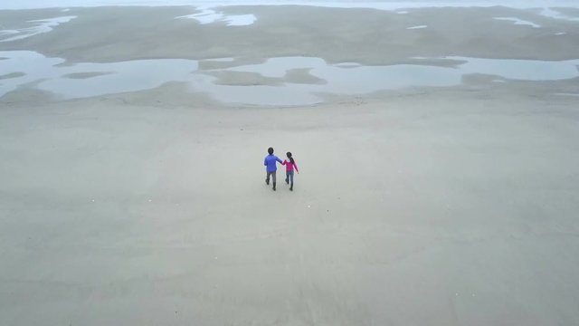 Father and daughter holding hands walking on the beach aerial footage