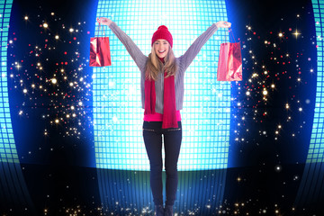 Festive blonde holding shopping bags against glittering screen on black background