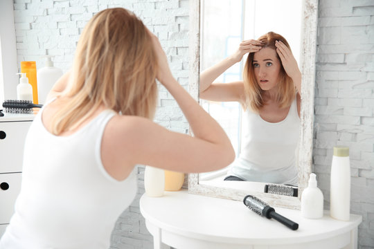 Young woman with hair loss problem in front of mirror at home