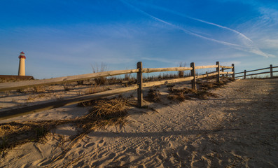 Fototapeta premium Wooden fence leads to beach near lighthouse in Cape May, NJ, on a sunny morning