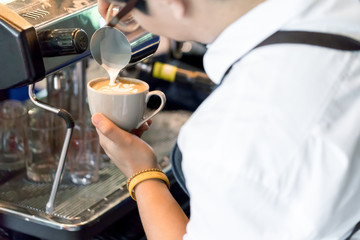 Close up of Asian barista holding a white cup making a latte art coffee in Coffee Shop. Preparation...