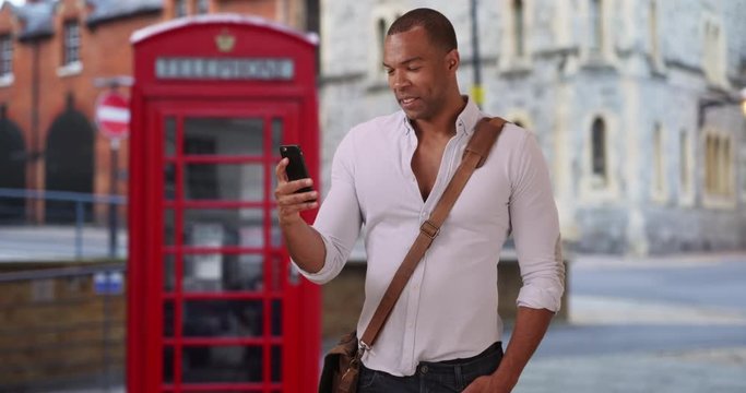 Young African male vacationing in England texting his friends back home on his smartphone, Good-looking Black man sends pictures of Windsor, England on his mobile device, 4k