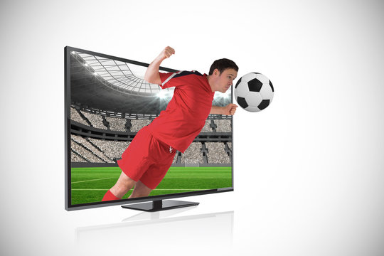 Composite image of football player in red heading ball through tv against vast football stadium with fans in white