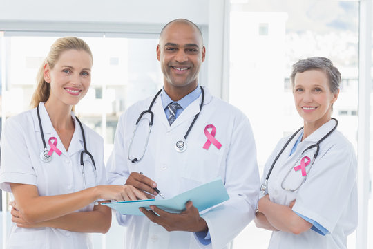 Pink breast cancer awareness ribbon against team of doctors working together on patients file