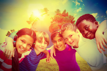 Happy children forming huddle at park against blue sky over green field