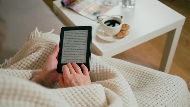 CloseUp to Ebook Reader in Hands of Adult Woman Sitting in a Cozy Room at Home with Coffee Cup