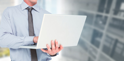 Businessman using a laptop against modern room overlooking city