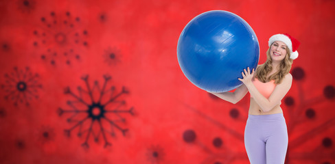 Naklejka premium Smiling blonde woman holding exercise ball against red snow flake background