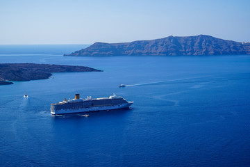 Large ferry ship and speed boats sailing on vast blue mediterranean sea with caldera mountain and...