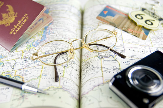 Eyeglasses, pen, passport book and camera on map