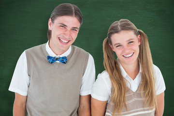 Smiling geeky hipsters looking at camera  against green chalkboard