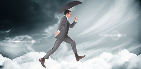 Fototapeta na wymiar Businessman jumping holding an umbrella against blue sky