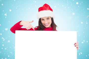 Pretty brunette in santa hat pointing white poster against blue vignette
