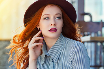 Stylish young beautiful red-haired girl in a burgundy hat in a street cafe - 203176160