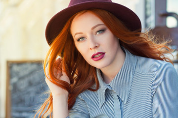 Stylish young beautiful red-haired girl in a burgundy hat in a street cafe - 203176186