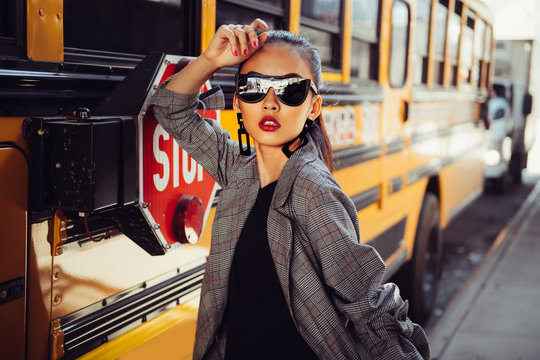 Beautiful fashionable Asian model girl wearing stylish black sunglasses posing outdoors on city street near bus