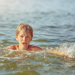 Happy little boy swimming in the river on summer weekend, image with square aspect ratio and warm...