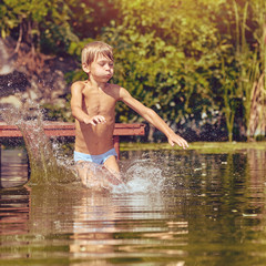 Little boy having fun and jumping into the river from pier, image with square aspect ratio and warm toning