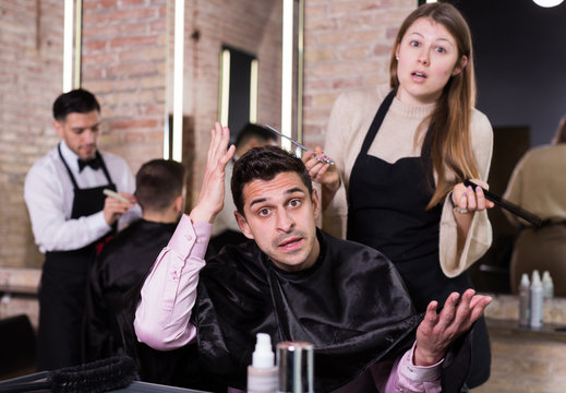 Shocked man with apologetic hairdresser at barbershop