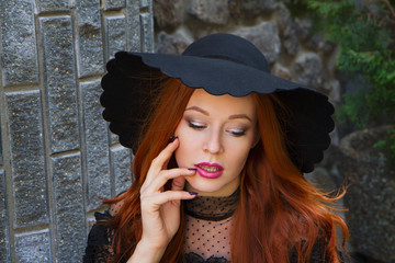portrait of stylish young beautiful red-haired girl in a black hat near the stone wall - 203177139