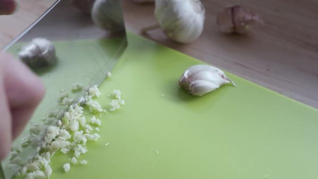 Lady prepare fresh chopped garlic using hand knife in the kitchen - close up food preparing concept