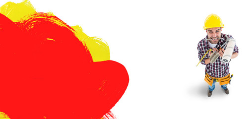 Frustrated handyman holding various tools against red and yellow paint 