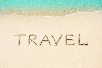 Travel word written on sand with soft ocean wave, beach background.