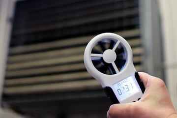Hand-held anemometer measuring air flowing of ventilation louvres of the industrial ventilation unit. - obrazy, fototapety, plakaty