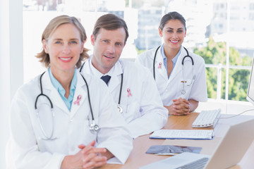 Fototapeta premium Smiling doctors posing at their desk wearing breast cancer awareness ribbon