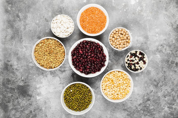 Assortment of beans (red lentil, green lentil, chickpea, peas, red beans, white beans, mix beans, mung bean) on gray background. Top view. Food background