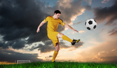 Football player in yellow kicking against green grass under blue and orange sky