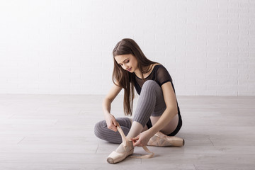 Beautiful ballet dancer sitting on the floor and prepare for performance and tie dance shoes