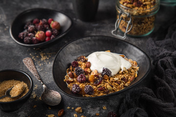 homemade granola (hazelnuts, raisin, dried cranberry, pumpkin, sesame and sunflower seeds) with yogurt in black bowl