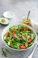 healthy vegan salad (tomatoes, avocado, cucumber, spinach and arugula) in white bowl