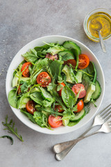 Fototapeta na wymiar healthy vegan salad (tomatoes, avocado, cucumber, spinach and arugula) in white bowl