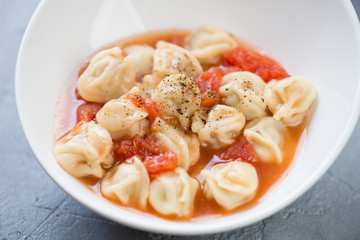Close-up of soup with ravioli served in a white bowl, selective focus, horizontal shot