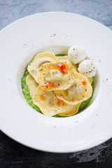 White plate with ravioli on a bed of green peas puree, selective focus, close-up