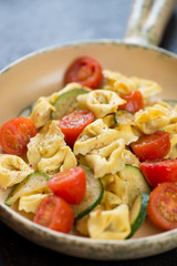 Close-up of italian tortellini served with fried zucchini and tomatoes, vertical shot, selective focus