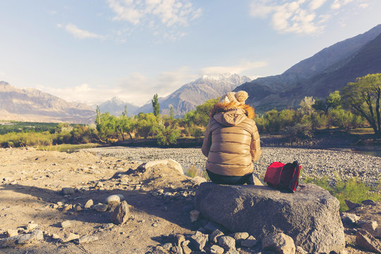 Young girl sitting on the rock relaxing see view in mountains with Cold weather, snow on hills.
