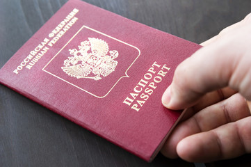 Male hand holding red passport. Grey wood background
